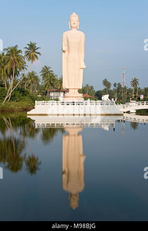 The Tsunami memorial in Hikkaduwa, Sri Lanka reflected in water in the late evening sun with blue sky. Stock Photo