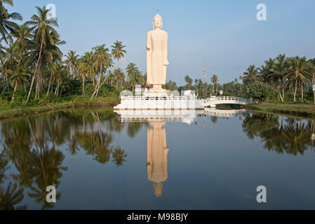 The Tsunami memorial in Hikkaduwa, Sri Lanka reflected in water in the late evening sun with blue sky. Stock Photo