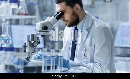 Research Scientist Adjusts Specimen in a Petri Dish and Looks on it Into Microscope. He's Working in a Modern Laboratory. Stock Photo