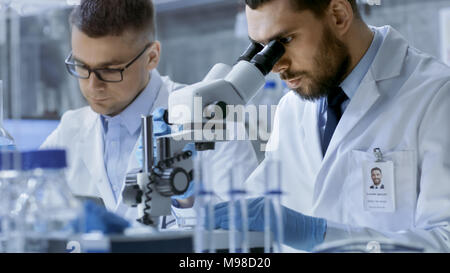 In a Modern Laboratory Two Scientists Conduct Experiments. Chief Research Scientist is Looking in a Microscope. Stock Photo