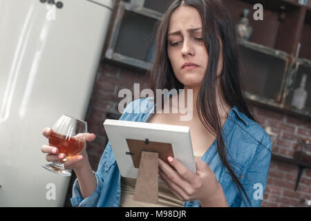 Young female alcoholic social problems standing holding frame looking at photo upset drinking whiskey Stock Photo