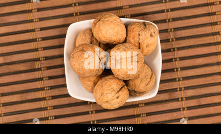 Pile of walnuts in a plate standing on a bamboo mat. View from above Stock Photo