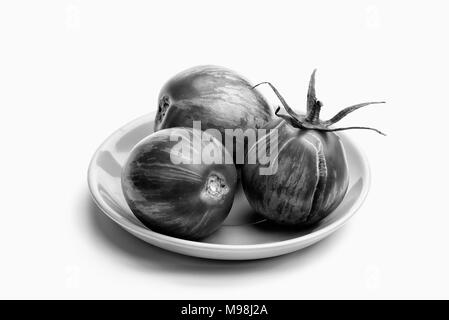 Three juicy zebra tomatoes in a little porcelain plate, isolated on white background Stock Photo