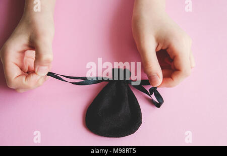 girl's hand holding a small black pouch for jewelry on a pink background, a surprise for a little Princess Stock Photo