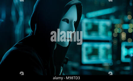 Masked Hacktivist Organizes malware Virus Attack on Global Scale. Hacker in Underground Secret Location Surrounded by Displays and Cables. Stock Photo