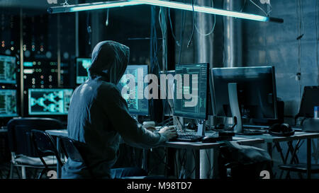 Hooded Hacker Using His Comuter with Different Information to Break into Corporate Data Servers and Infects them with Virus. Dark Hideout Place. Stock Photo