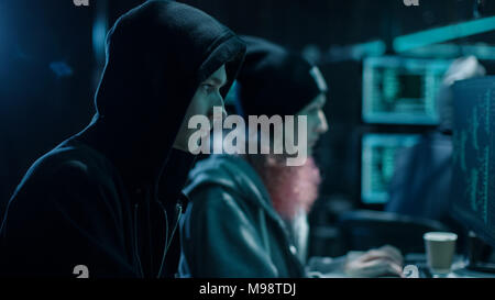 Close-up Shot of Internationally Wanted Boy and Girl Hackers Team Working on Their Computers. Place is Hacker's Den with Dark atmosphere. Stock Photo