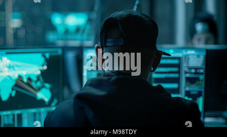 Close-up Frame from the Back of Working Hacker Organizing Advanced Virus Attack on Corporate Servers. Place is Dark and Has Multiple displays. Stock Photo