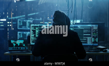 Dangerous Hooded Hacker Breaks into Government Data Servers and Infects Their System with a  Virus. His Hideout Place has Dark Atmosphere Stock Photo