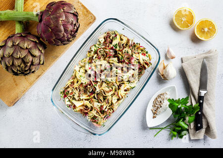 Carpaccio from Fresh big Romanesco artichokes green-purple flower heads in glass refractory baking tray Stock Photo