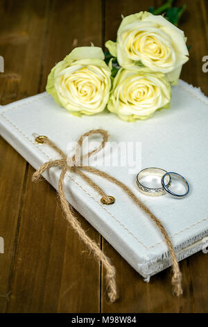 pair of wedding rings on white journal with string bow and rose bouquet Stock Photo