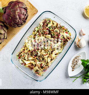 Carpaccio from Fresh big Romanesco artichokes green-purple flower heads in glass refractory baking tray Stock Photo