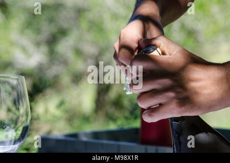 Preparing to pop open a bottle of sparkling wine outside. Closeup of hands preparing to open champagne bottle in outdoors celebration. Stock Photo