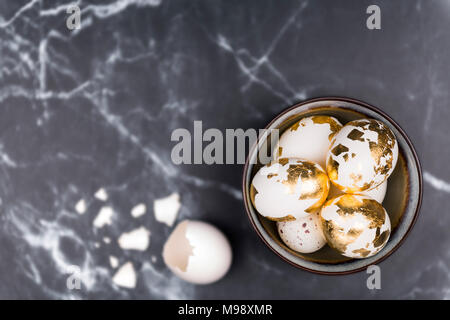 Feminine stylish background, white eggs decorated with golden foil in rustic bowl, and broken egg shell. Space for text on black marble background. Stock Photo