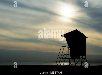 silhouette of lifeguard tower on a California beach under smoky skies with sun pushing through Stock Photo