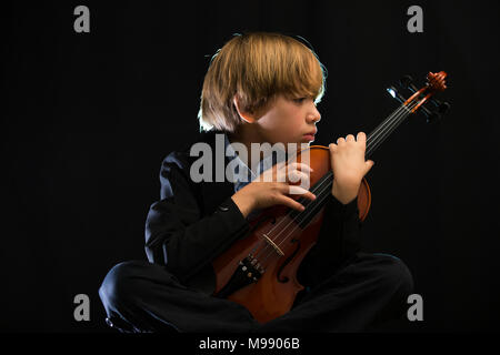 child playing violin, black background, sentimental theme, sad, pensive, concentrated Stock Photo