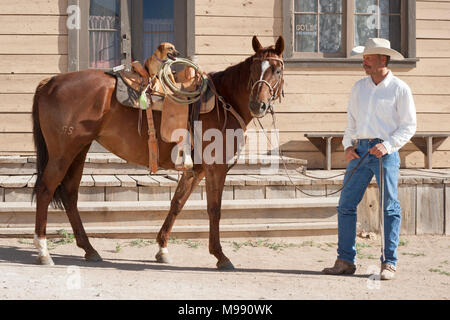 Cowboy with his horse and Jack Russell Terrier sitting in the saddle in old west town Stock Photo