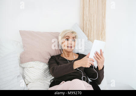 An older positive woman uses a tablet to watch videos, listen to music and chat with friends on social networks. Stock Photo