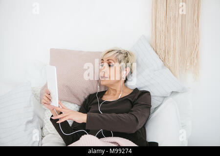 An older positive woman uses a tablet to watch videos, listen to music and chat with friends on social networks. Stock Photo