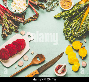 Colorful beetroot cooking preparation. Red and yellow sliced beetroot, chard  leaves and ingredients on light blue kitchen table background, top view, Stock Photo