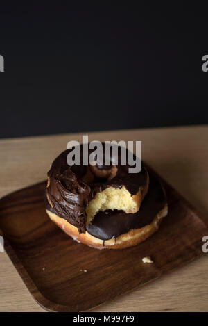 Chocolate Iced Doughnuts with a Bite Missing in front of a Dark Background Stock Photo