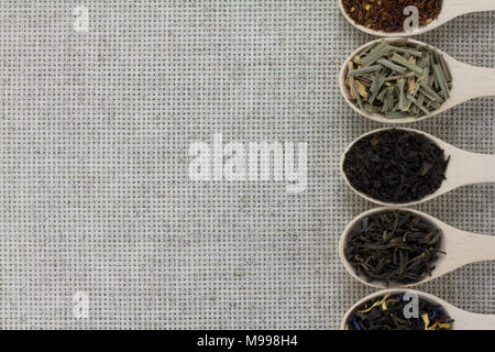 Assortment of different types of tea in a wooden spoon on a background of gray natural fabric Stock Photo