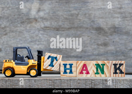 Yellow plastic forklift hold letter T to complete word thank on wood background Stock Photo