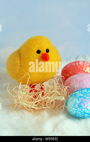 yellow small baby chick inside a nest with three colorful eggs in a vertical format with a cloud background with bright colored eggs and white bottom Stock Photo