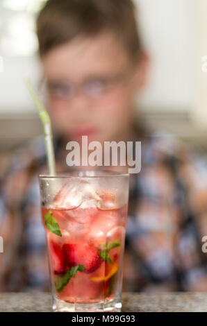 Hot summer vacation concept. Refreshing mint cocktail on a cafe table with a blurred teenage boy reading in the background. Stock Photo