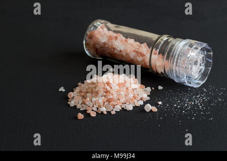 Salt on black background with commercial salt grinder and heap of pink and orange salt Himalayan crystals - Space for text Stock Photo