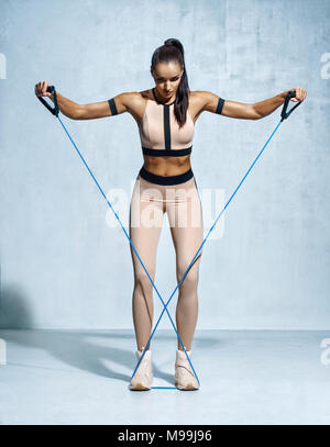 Fitness girl performs exercises with resistance band. Photo of fitness model workout on grey background. Strength and motivation Stock Photo