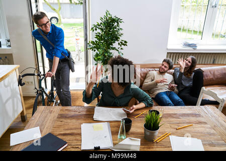 Coworkers waving at young man with bicycle arriving in modern office Stock Photo