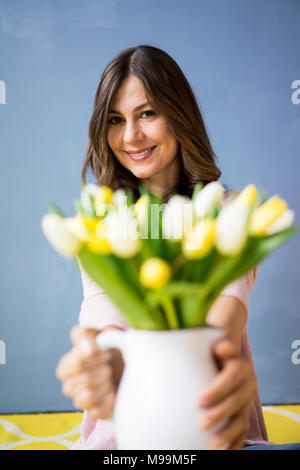 Portrait of smiling woman holding bunch of tulips in a jar Stock Photo