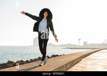 Spain, Barcelona, woman wearing hooded jacket balancing on promenade Stock Photo