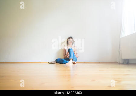 Smiling mature woman sitting on floor in empty room using tablet Stock Photo