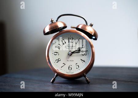 An old fashioned copper coloured bed side analogue pre digital alarm clock, made by the Towcester Clock Works, UK Stock Photo