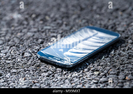 Asphalt pavement road with broken phone smartphone, cracked screen fell on ground Stock Photo