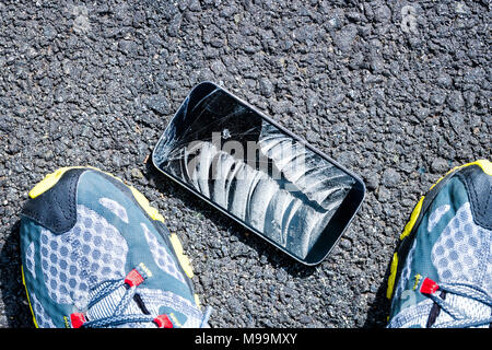 Looking down on asphalt pavement road with broken phone smartphone screen, Man, fell on ground, shoes sneakers flat top view down lay Stock Photo