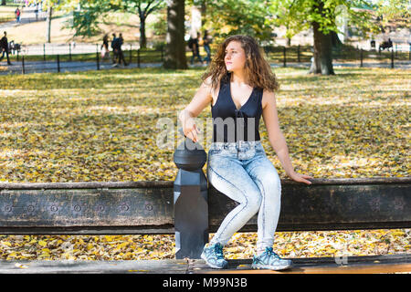 Manhattan New York City NYC Central park with trees, young hipster millennial woman sitting on bench, many fallen leaves in autumn fall season with ye Stock Photo