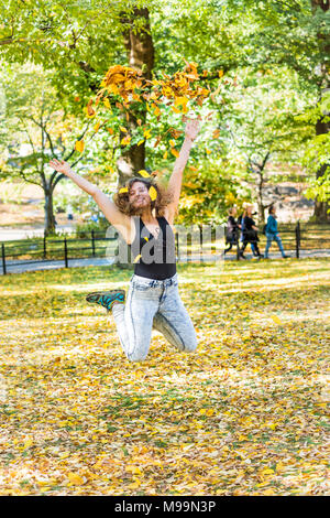 Manhattan New York City NYC Central park, young hipster millennial woman jumping, many fallen leaves up in air falling in autumn fall season with yell Stock Photo
