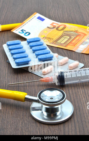 Stethoscope with pills, money and syringe on a wooden desk Stock Photo