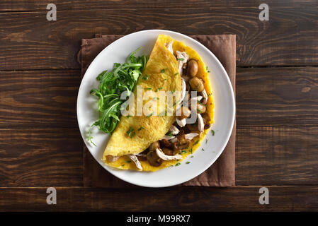 Healthy food for breakfast. Omelette stuffed with mushrooms, pieces of chicken meat, greens on wooden table. Top view, flat lay