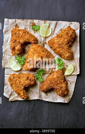 Spicy fried breaded chicken wings on paper over dark black background. Top view, flat lay Stock Photo