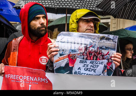 Barcelona, Catalonia, Spain. 24th Mar, 2018. Two activists of Open Arms seen displaying posters. Open Arms has gathered hundreds of people outside the Barcelona Italian Embassy in protest at the retention of one of its rescue boats and the serious allegations by Sicilian prosecutors.The direction of Open Arms is facing 15 years in prison and heavy fines for doing their job saving lives following allegations of prosecutors of Sicily (Italy) for trafficking and criminal association. Credit: Paco Freire/SOPA Images/ZUMA Wire/Alamy Live News Stock Photo