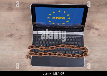 Laptop with GDPR letters in EU stars on wood background. Keyboard locked by old rusty chains. Personal data protection, digitization and bureaucracy. Stock Photo