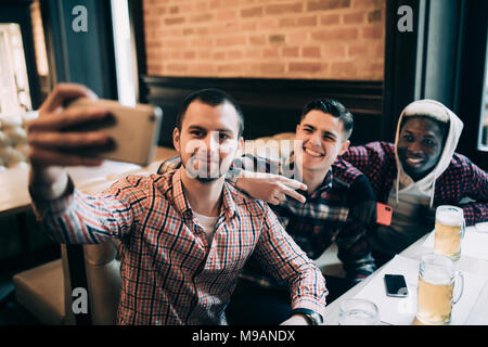 people, leisure, friendship, technology and bachelor party concept - happy male friends taking selfie and drinking beer at bar or pub Stock Photo