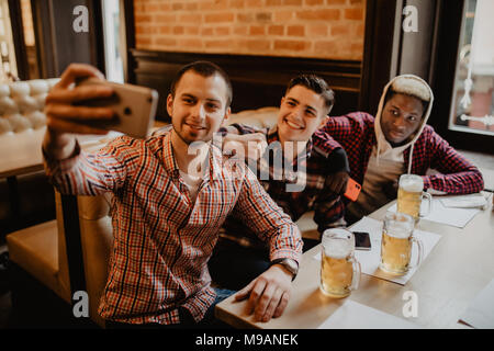 people, leisure, friendship, technology and bachelor party concept - happy male friends taking selfie and drinking beer at bar or pub Stock Photo