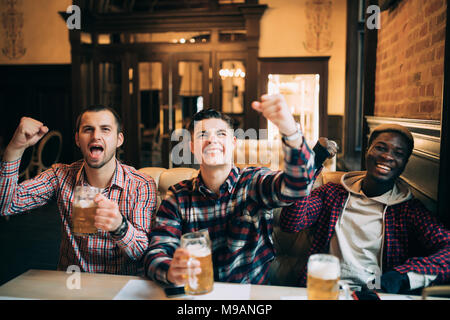 Happy football fans or male friends drinking beer and celebrating victory at bar or pub Stock Photo