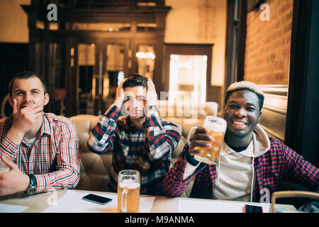 Watching TV in bar. Two happy young men drinking beer and gesturing while sitting in bar Stock Photo