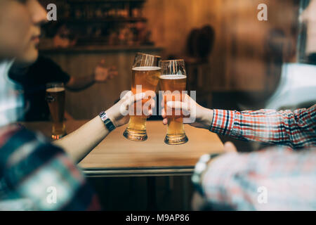 Close up friends sitting at the pub cheers with beers glasses trough window. Stock Photo